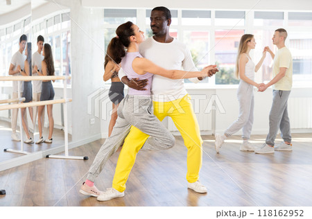 Happy African american man in pair with young woman dancing and training latin dance movements in ballroom together Happy African american man in pair with young woman dancing and training latin dance movements in ballroom together 118162952