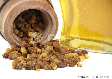 Close-up of a natural bee bread spilling from a wooden barrel against a white background Close-up of a natural bee bread spilling from a wooden barrel against a white background 118163456