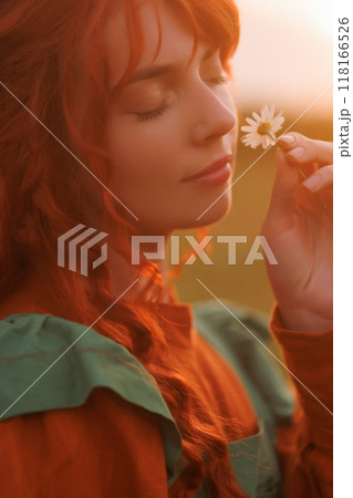 A shepherdess woman with red hair and a green dress in a field on sunset. A shepherdess woman with red hair and a green dress in a field on sunset. 118166526