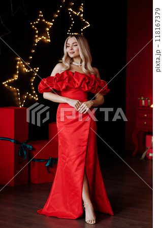 A woman in a red dress stands in front of a Christmas tree. Full length. 118167379