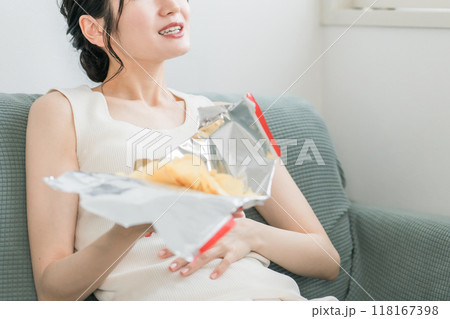 自宅のソファでポテトチップスを食べる若いアジア人女性（間食・栄養バランス・生活習慣病・高カロリー） 118167398