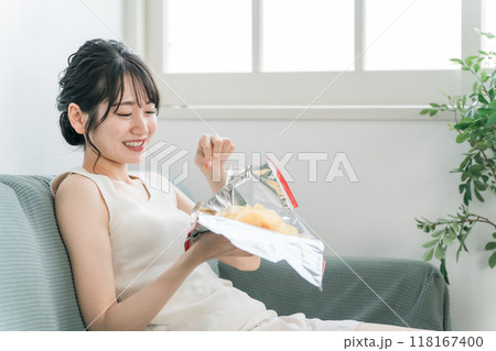 自宅のソファでポテトチップスを食べる若いアジア人女性（食生活・間食・栄養バランス・生活習慣病） 118167400