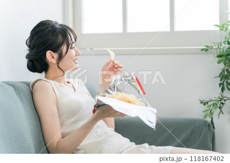 自宅のソファでポテトチップスを食べる若いアジア人女性（暴飲暴食・間食・高カロリー） 118167402