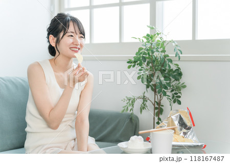 自宅のソファでポテトチップスを食べる若いアジア人女性（暴飲暴食・間食・高カロリー） 118167487