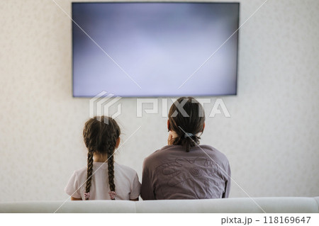 Back view of teenage boy with his six year old sister watching TV in living room. Big screen  118169647