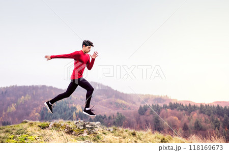 Male runner jumping over rock, jogging in nature on dirt running trail. Morning running training for young man. Male runner jumping over rock, jogging in nature on dirt running trail. Morning running training for young man. 118169673