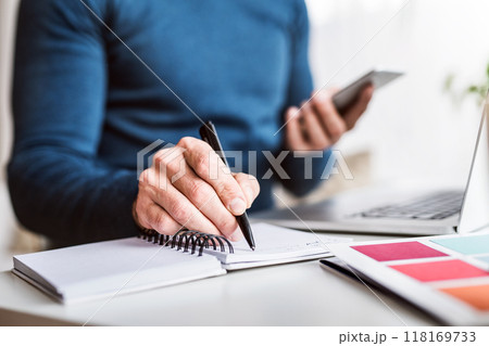 Close up of man writing notes in planner, working at desk from home. Telecommuting and home office. Close up of man writing notes in planner, working at desk from home. Telecommuting and home office. 118169733