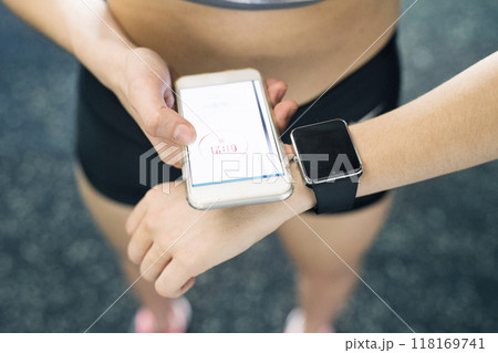 Young fitness girl checking her performance on smatphone and smartwatch after hard workout in gym. Young fitness girl checking her performance on smatphone and smartwatch after hard workout in gym. 118169741