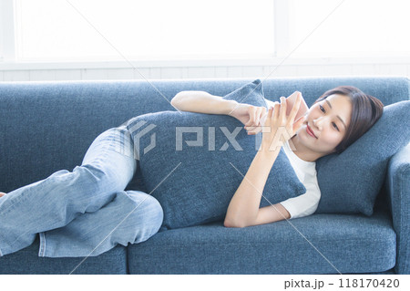 ソファに寝転がってスマホを持つ女性 118170420