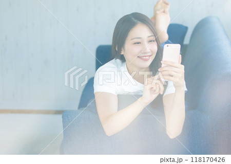 ソファに寝転がってスマホを持つ女性 ソファに寝転がってスマホを持つ女性 118170426