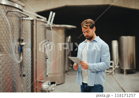 The winemaker standing in the wine cellar, monitoring the fermentation and aging processes in large barrels. 118171257