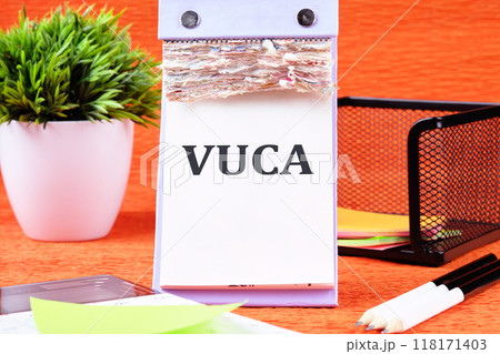 Volatility Uncertainty Complexity Ambiguity. VUCA text on a blank desktop calendar page on an orange background Volatility Uncertainty Complexity Ambiguity. VUCA text on a blank desktop calendar page on an orange background 118171403