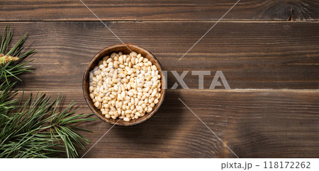 Pine nuts in a bowl on a brown wooden background with a branch of pine needles. Healthy diet snack.  118172262