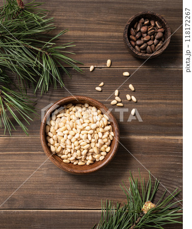 Pine nuts in a bowl and a handful of unpeeled nuts on a brown wooden background  118172267