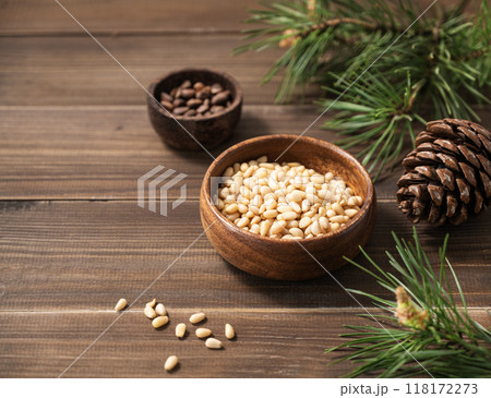 Pine nuts in a bowl and a handful of unpeeled nuts on a brown wooden background Pine nuts in a bowl and a handful of unpeeled nuts on a brown wooden background 118172273