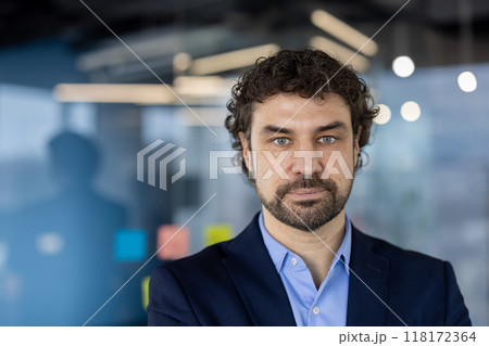 Businessman with serious expression standing in modern office setting, showcasing confidence and professionalism. Portrait reflects thoughtful attitude, suitable for corporate environments 118172364