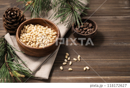 Pine nuts in a bowl on napkin and a handful of unpeeled nuts on a brown wooden background Pine nuts in a bowl on napkin and a handful of unpeeled nuts on a brown wooden background 118172627