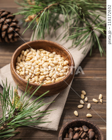 Pine nuts in a bowl on napkin and a handful of unpeeled nuts on a brown wooden background Pine nuts in a bowl on napkin and a handful of unpeeled nuts on a brown wooden background 118172632