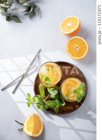 Freshly squeezed juice in a glass with fresh oranges, mint and ice on a light background Freshly squeezed juice in a glass with fresh oranges, mint and ice on a light background 118172971