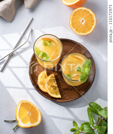Freshly squeezed juice in a glass with fresh oranges, mint and ice on a light background  118172973