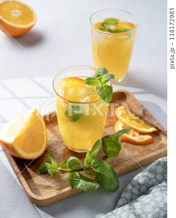 Freshly squeezed juice in a glass with fresh oranges, mint and ice on a light background 118172985