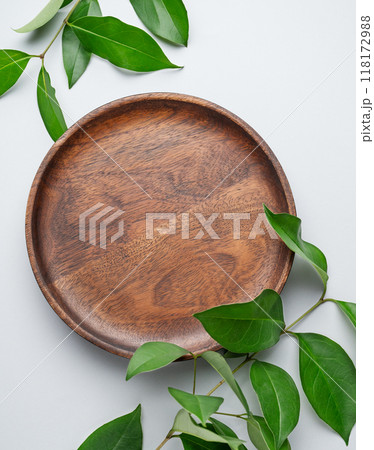 Modern empty product display. Minimal wooden round plate with green leaves on a gray background Modern empty product display. Minimal wooden round plate with green leaves on a gray background 118172988
