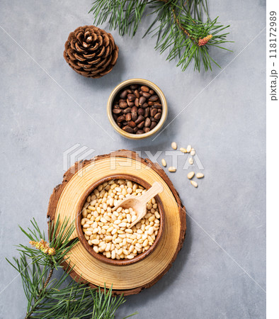 Pine nuts in a bowl on a board and scattered on a blue background with branches of pine needles  118172989