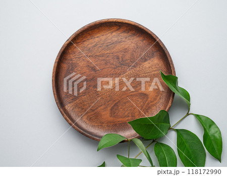Modern empty product display. Minimal wooden round plate with green leaves on a gray background.  118172990