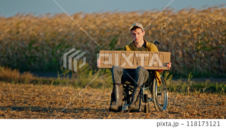 A man in a wheelchair holding a HELP NEEDED sign in a dry field at sunset. A man in a wheelchair holding a HELP NEEDED sign in a dry field at sunset. 118173121