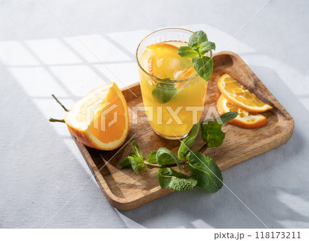 Orange juice with fresh fruits, mint and ice on a light background with shadow.  118173211