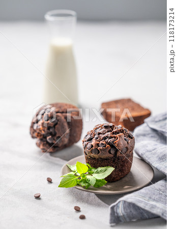Chocolate muffins on a white plate with mint on a light background with milk. 118173214