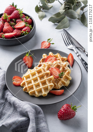 Homemade soft waffles with fresh strawberries in a plate on a light background. Homemade soft waffles with fresh strawberries in a plate on a light background. 118173217