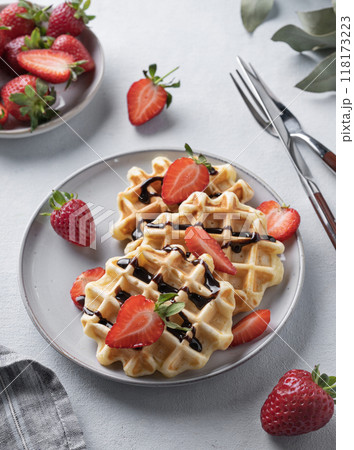 Homemade soft waffles with fresh strawberries and chocolate topping in a plate on a light background Homemade soft waffles with fresh strawberries and chocolate topping in a plate on a light background 118173223