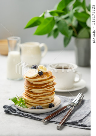 A stack of oat banana pancakes with fresh fruit slices, berries and honey on a light background 118173228