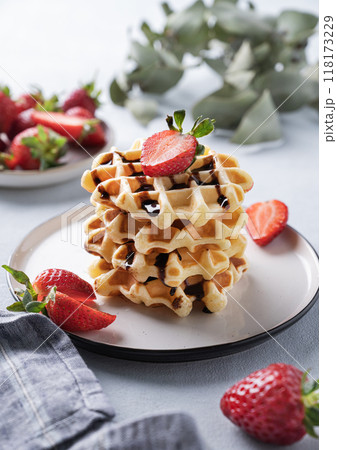 Homemade soft waffles with fresh strawberries and chocolate topping in a stack in a plate  118173229
