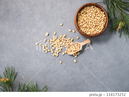 Pine nuts in a bowl  and a scattered on a blue background with branches of pine needles.  118173252