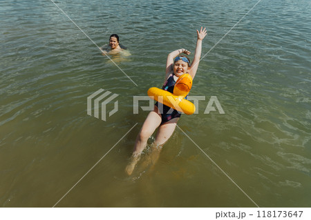 A girl is swimming with an inflatable yellow duck in the lake under her mother's supervision. She is enjoying a safe summer swim while her mother ensures her safety and care 118173647