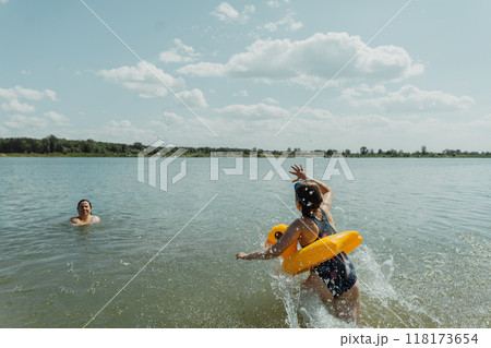 A happy child with an inflatable yellow duck is splashing in the lake on a bright summer day. She is having fun and enjoying her vacation A happy child with an inflatable yellow duck is splashing in the lake on a bright summer day. She is having fun and enjoying her vacation 118173654