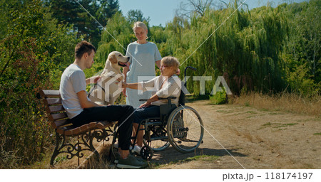 A family with a dog spending time outdoors, including a woman in a wheelchair and two other adults. 118174197
