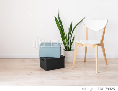 White wooden chair, cardboard boxes and a houseplant in a pot on a beige oak floor and gray wall 118174425