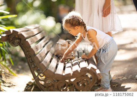 Little girl playing on a bench in a park Little girl playing on a bench in a park 118175002