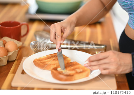 Close up shot of woman spreading butter on toasted bread with a cutlery knife 118175410