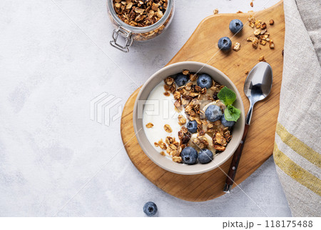 The concept of a healthy breakfast of yogurt, granola and fresh blueberry on a light background. The concept of a healthy breakfast of yogurt, granola and fresh blueberry on a light background. 118175488