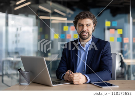 Confident businessman working on laptop in modern office. Business professional seated at desk with tablet and holding pen, ready for business meeting. 118175652