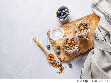 Homemade baked granola with nuts and fresh blueberry in a jar on a light background. 118175964