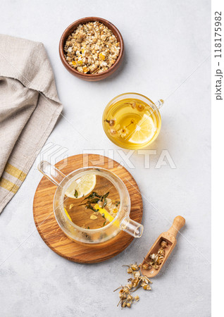 Chamomile herbal tea with lemon in a glass cup and teapot with flowers on a light background. Chamomile herbal tea with lemon in a glass cup and teapot with flowers on a light background. 118175982