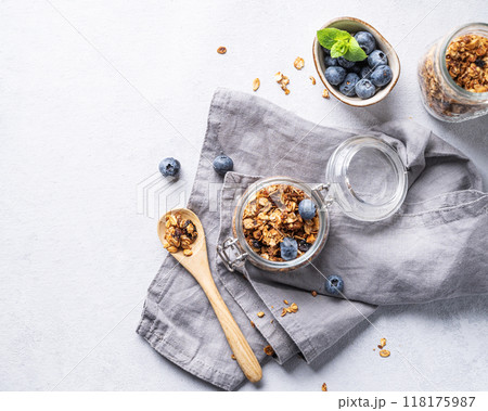 Homemade baked granola with nuts and fresh blueberry in a jar on a light background with napkin. Homemade baked granola with nuts and fresh blueberry in a jar on a light background with napkin. 118175987