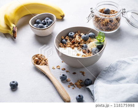 Homemade baked granola with yogurt, blueberries and banana in a bowl on a light background Homemade baked granola with yogurt, blueberries and banana in a bowl on a light background 118175998
