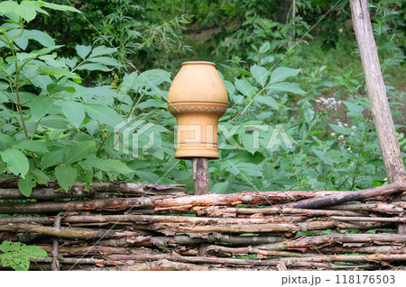 Retro design. Clay jug on a wicker fence in countryside. Terracotta pot. 118176503