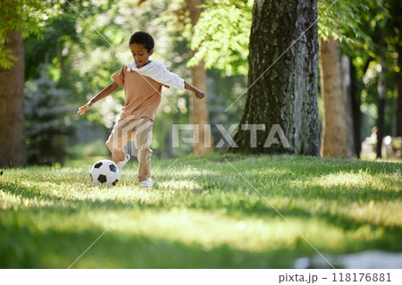 Little African American boy improving football skill during warm summer day in park 118176881